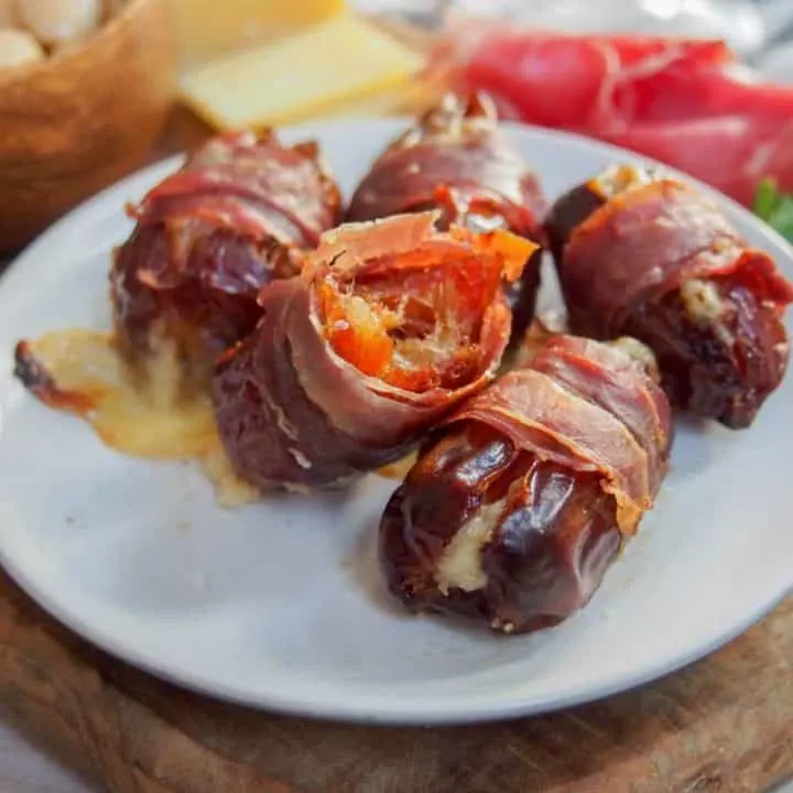 close up of prosciutto wrapped dates on a white plate