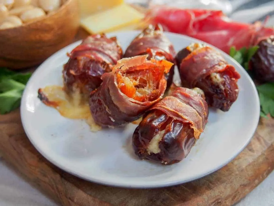 close up of prosciutto wrapped dates on a white plate