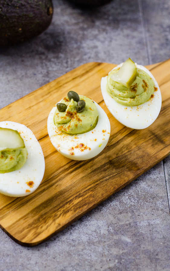 three hard boiled eggs with avocado on a wood plate