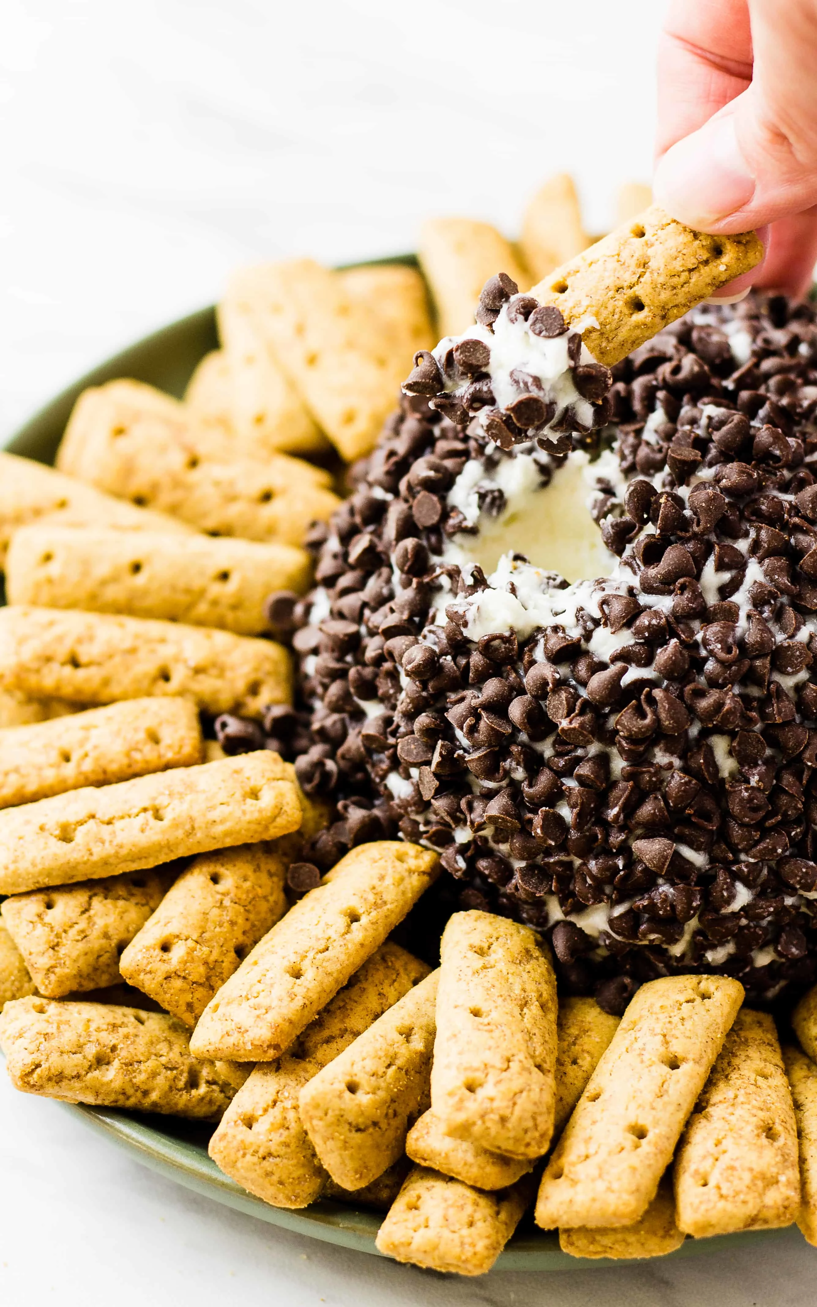 hand dipping graham cracker stick in to Cannoli Cheese Ball