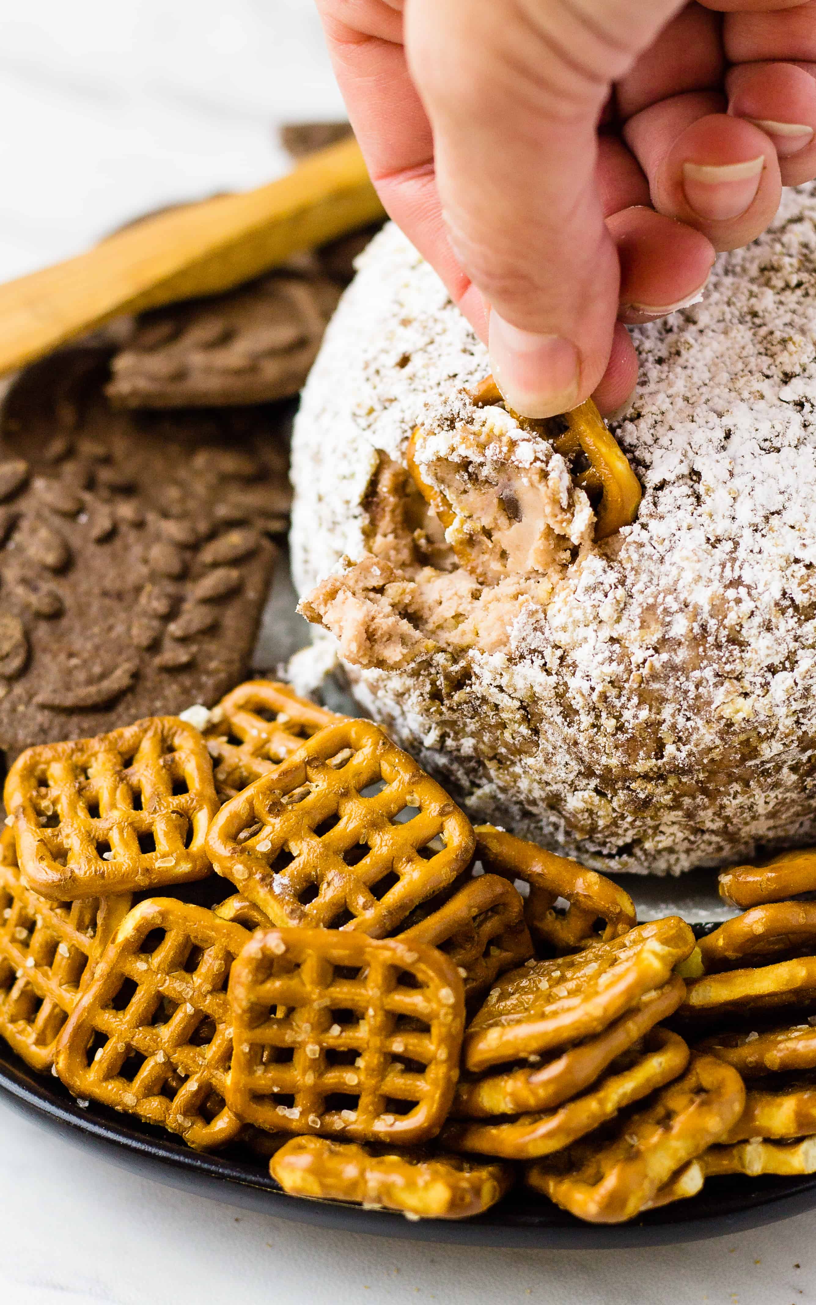 Hand dipping a Salted pretzels in to the cheese ball