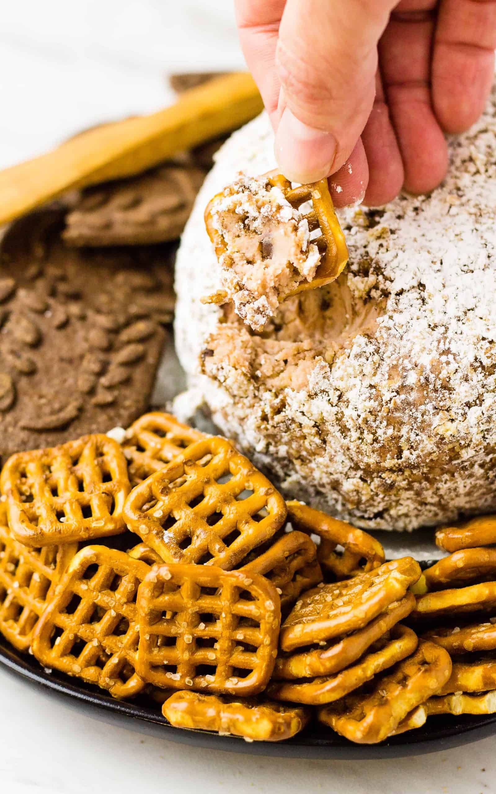 Hand with a recently dipped Salted pretzel and the cheese ball