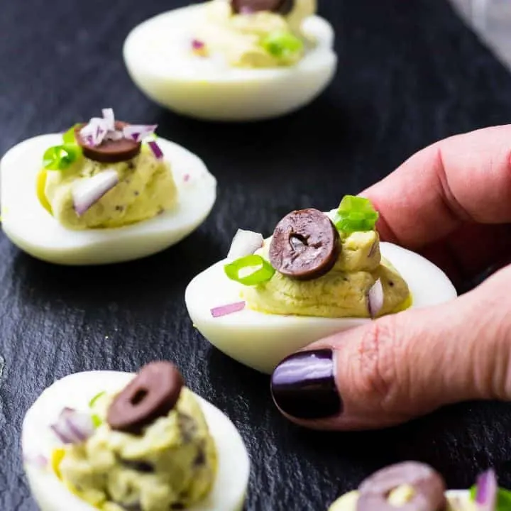 Hand holding a Mediterranean Deviled Egg with others on a black wooden platter