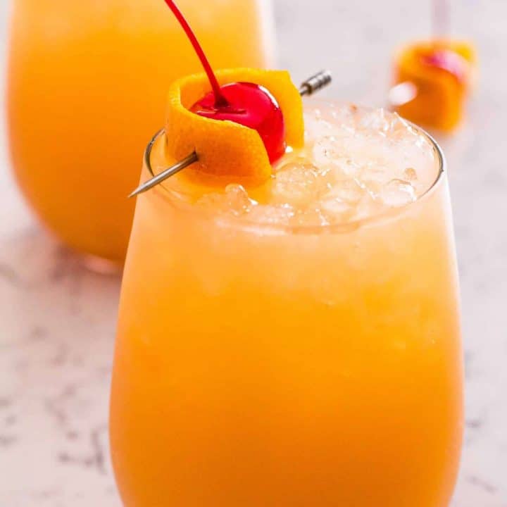 Side view of orange cocktail with cherry garnish in a wine glass