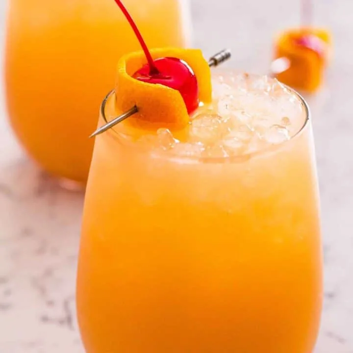 Side view of orange cocktail with cherry garnish in a wine glass