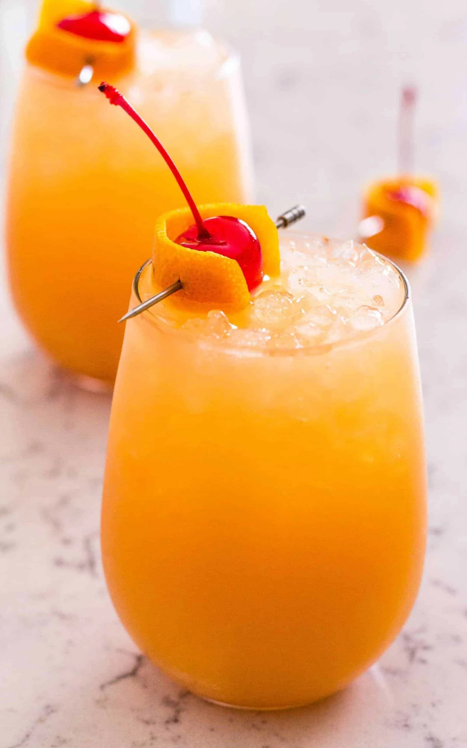 Side view of orange cocktail with cherry garnish in a wine glass