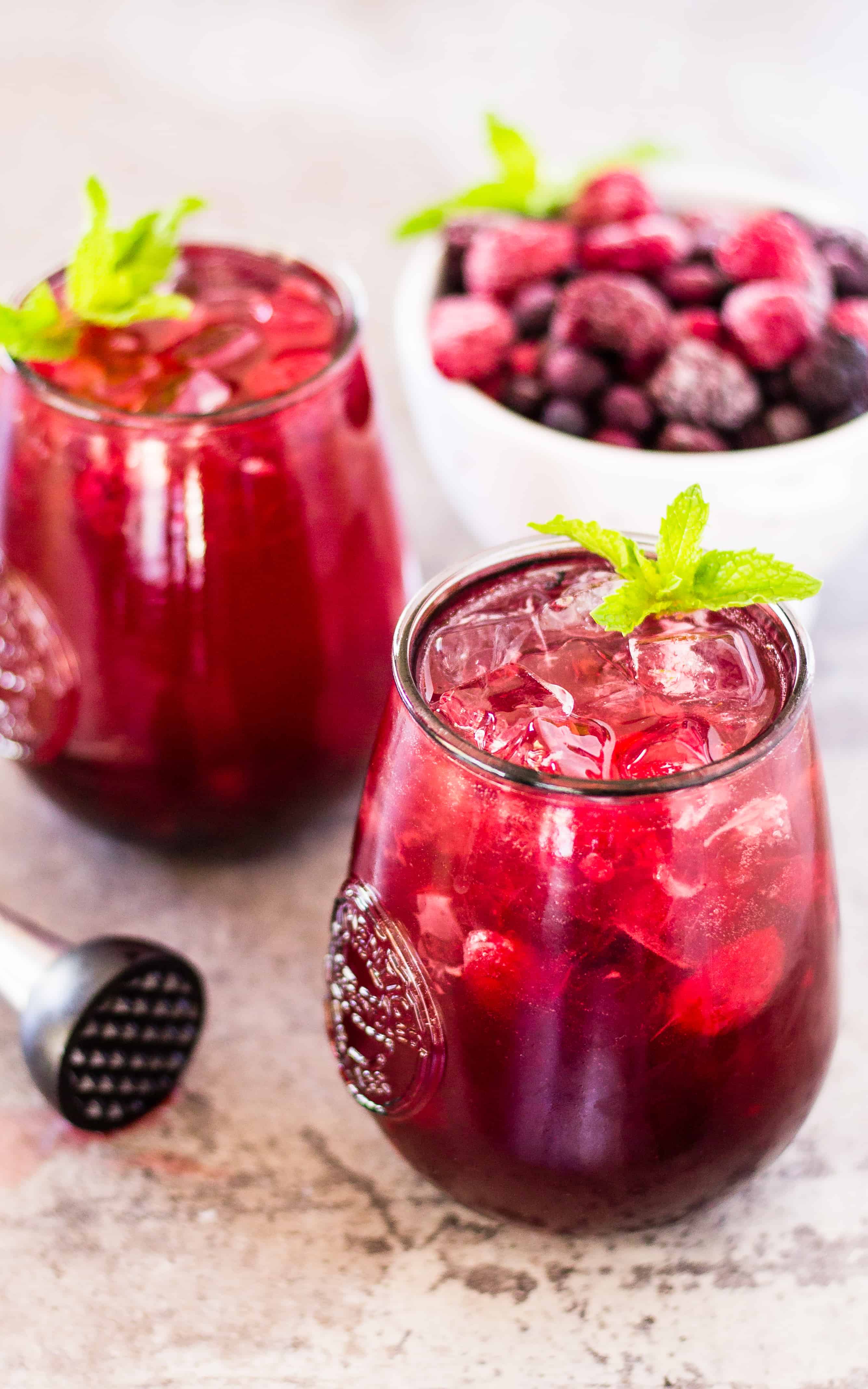 Side view of 2 skinny sangria spritzers and a bowl of berries on a table