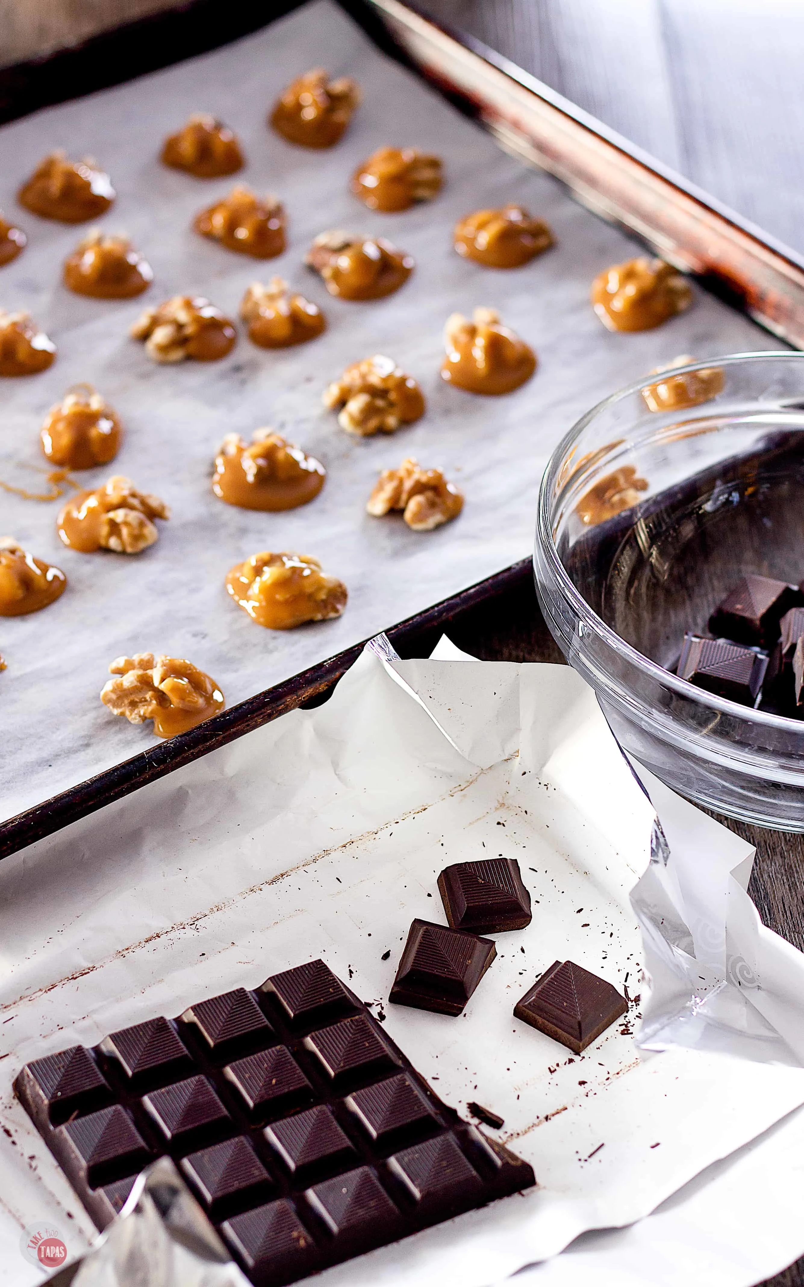 Dark chocolate dusted with pink sea salt being broken in to pieces with the caramel coated walnuts in the background