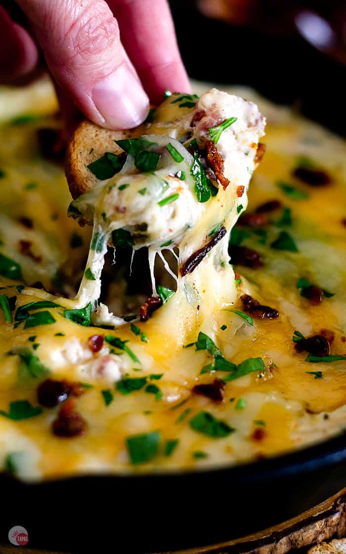 close up of Kentucky Hot Brown Dip in a Skillet with a hand dipping a chip in it