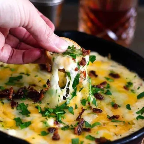 Hot Brown Skillet Dip with a hand dipping a chip in it