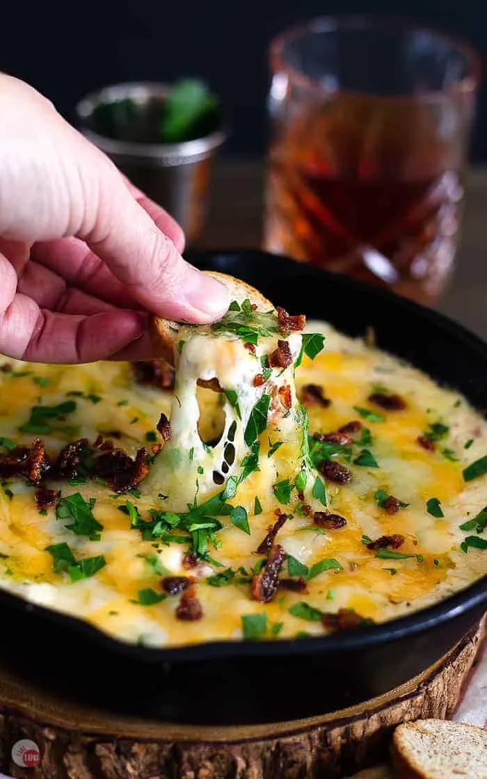 Hot Brown Skillet Dip with a hand dipping a chip in it