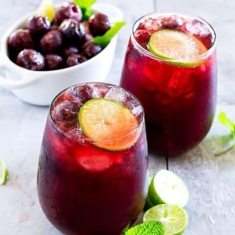 Side angle picture of wine glasses with cherry limeade punch and a bowl of frozen cherries