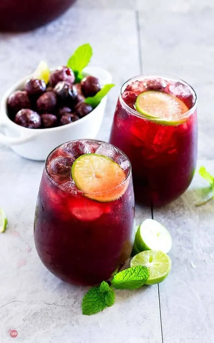 Side angle picture of wine glasses with cherry limeade punch and a bowl of frozen cherries