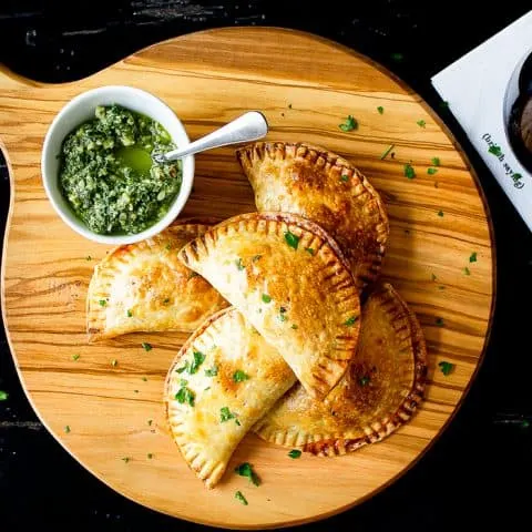 empanadas on a serving board on black table with a drink