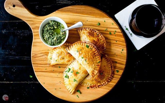 empanadas on a serving board on black table with a drink