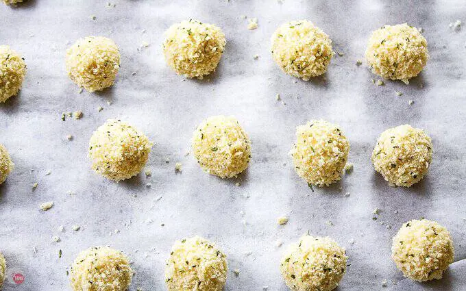 arancini rolled in panko crumbs on a baking sheet