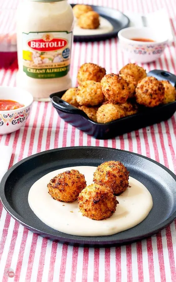 table set with cheesy alfredo arancini balls on small black plates