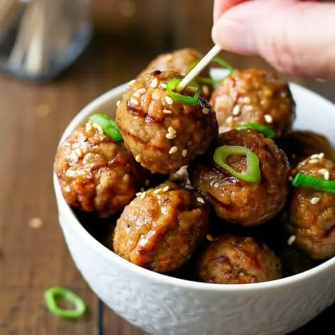 close up of cooked pineapple ginger meatballs with hand holding toothpick in meatball
