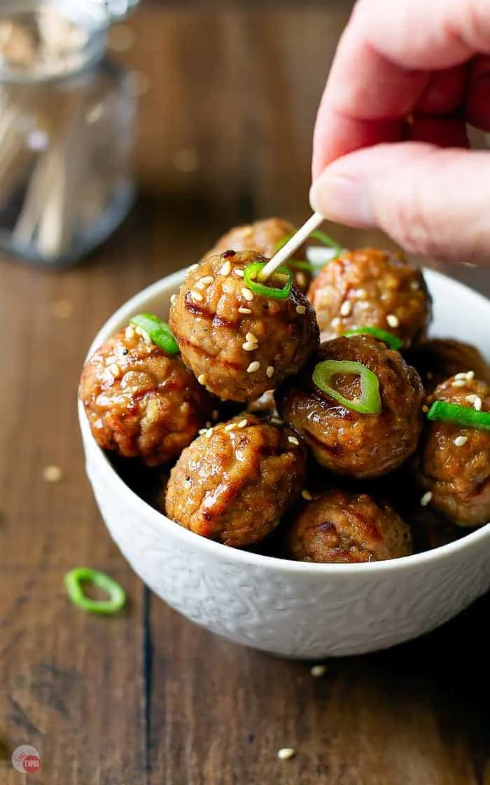 close up of cooked pineapple ginger meatballs with hand holding toothpick in meatball