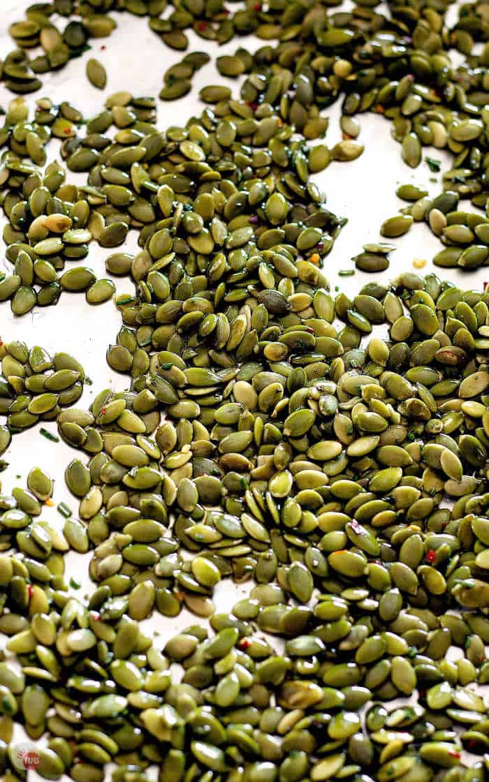 spreading rosemary pumpkin seeds on a baking sheet