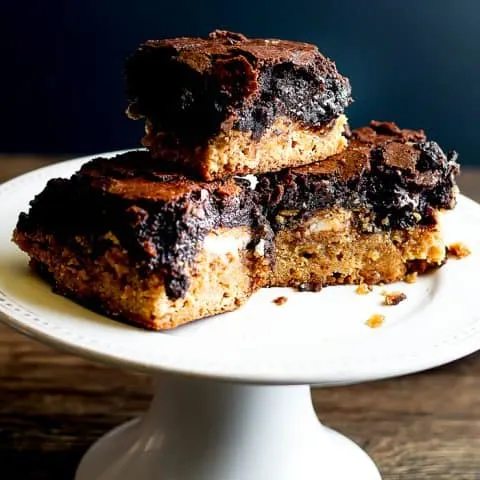 three brownies on a white cake stand on a wood board with black background