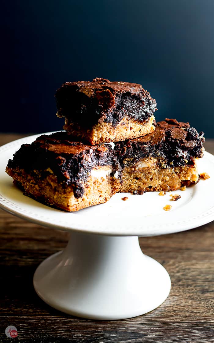 three brownies on a white cake stand on a wood board with black background