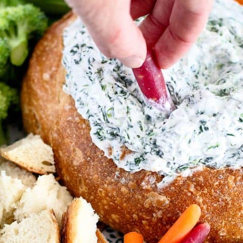 Spinach dip in bread bowl with hand dipping carrot in it