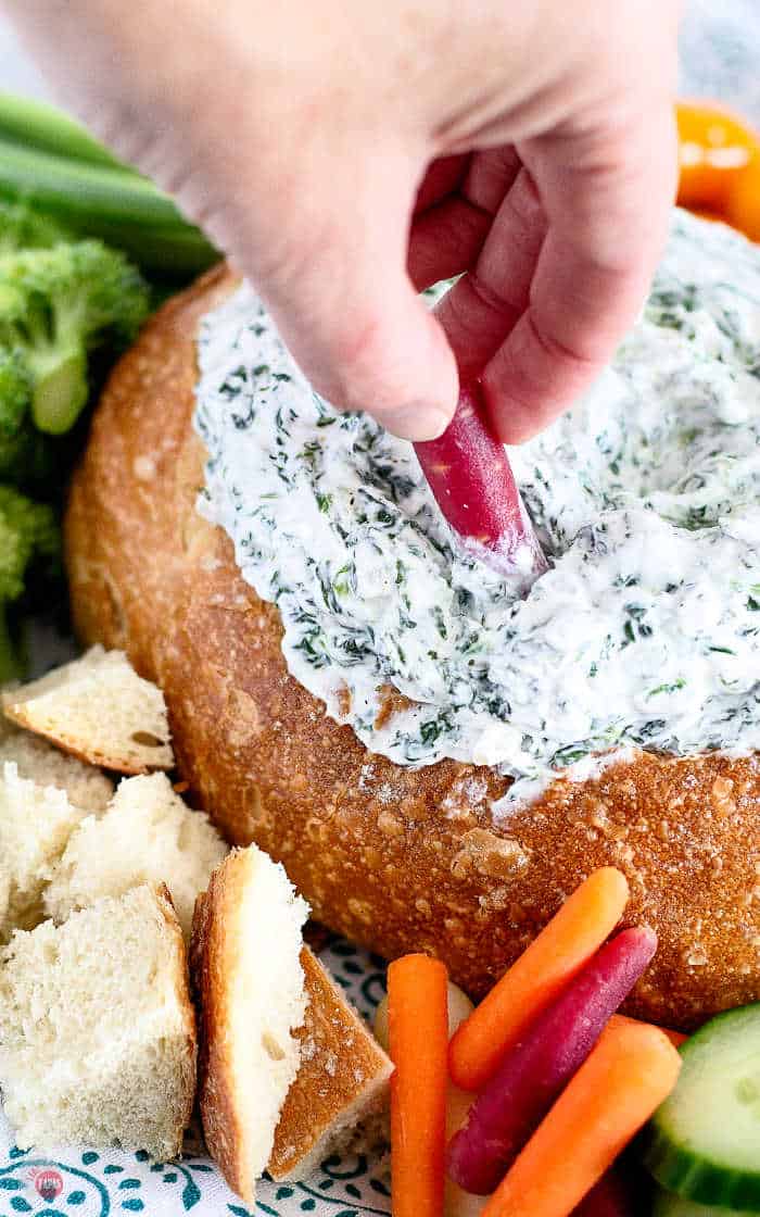 Spinach dip in bread bowl with hand dipping carrot in it