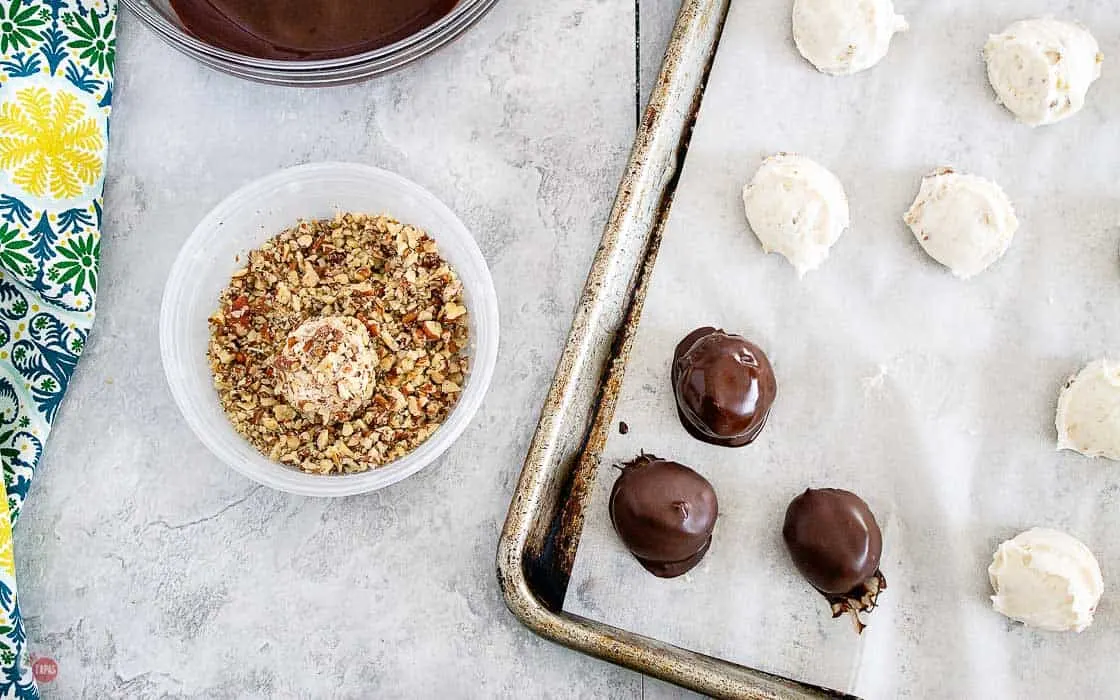 truffles dipped in chocolate and rolled in pecans on a baking sheet