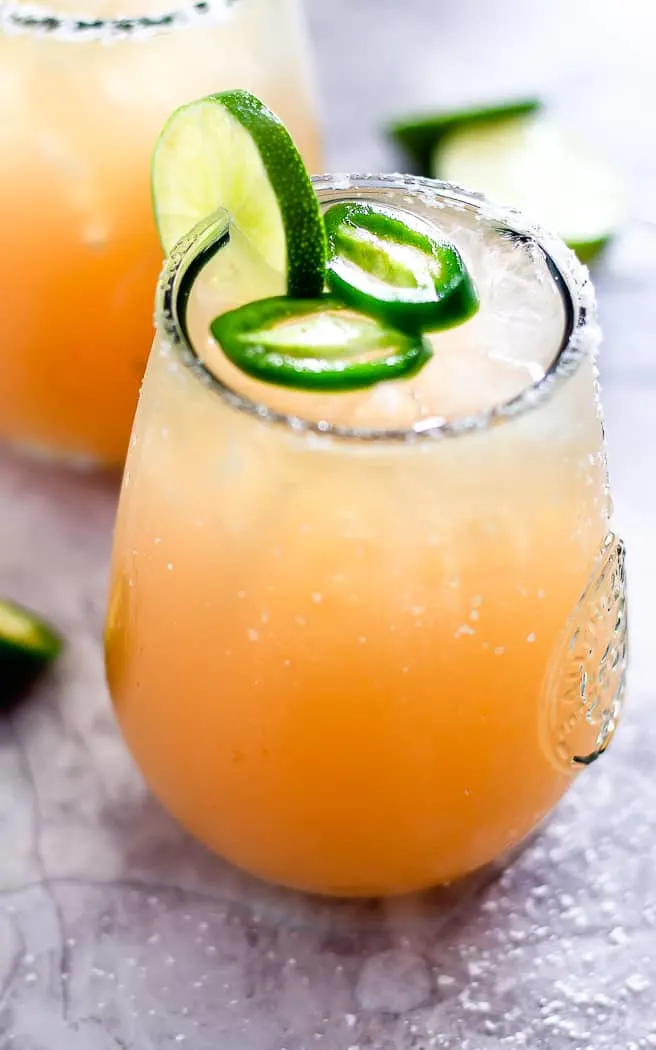 closeup of a paloma drink with jalapeno slices on top and a lime garnish