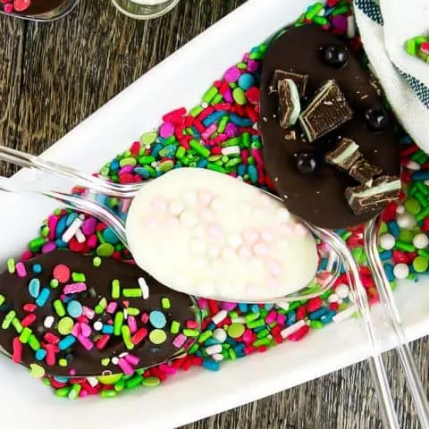 chocolate dipped spoons on a while platter covered in sprinkles