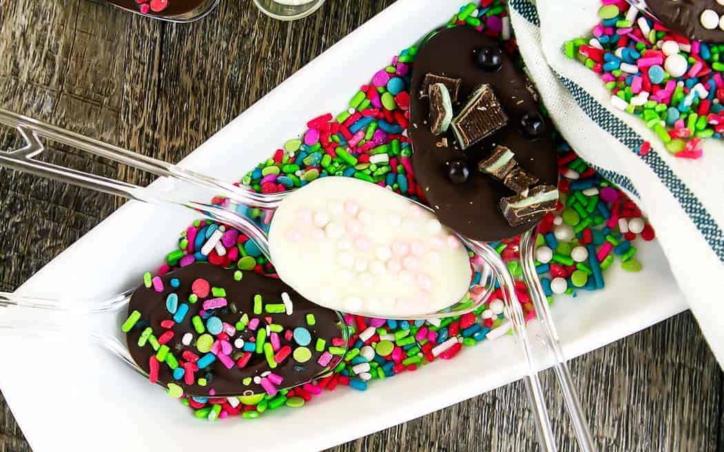 chocolate dipped spoons on a while platter covered in sprinkles