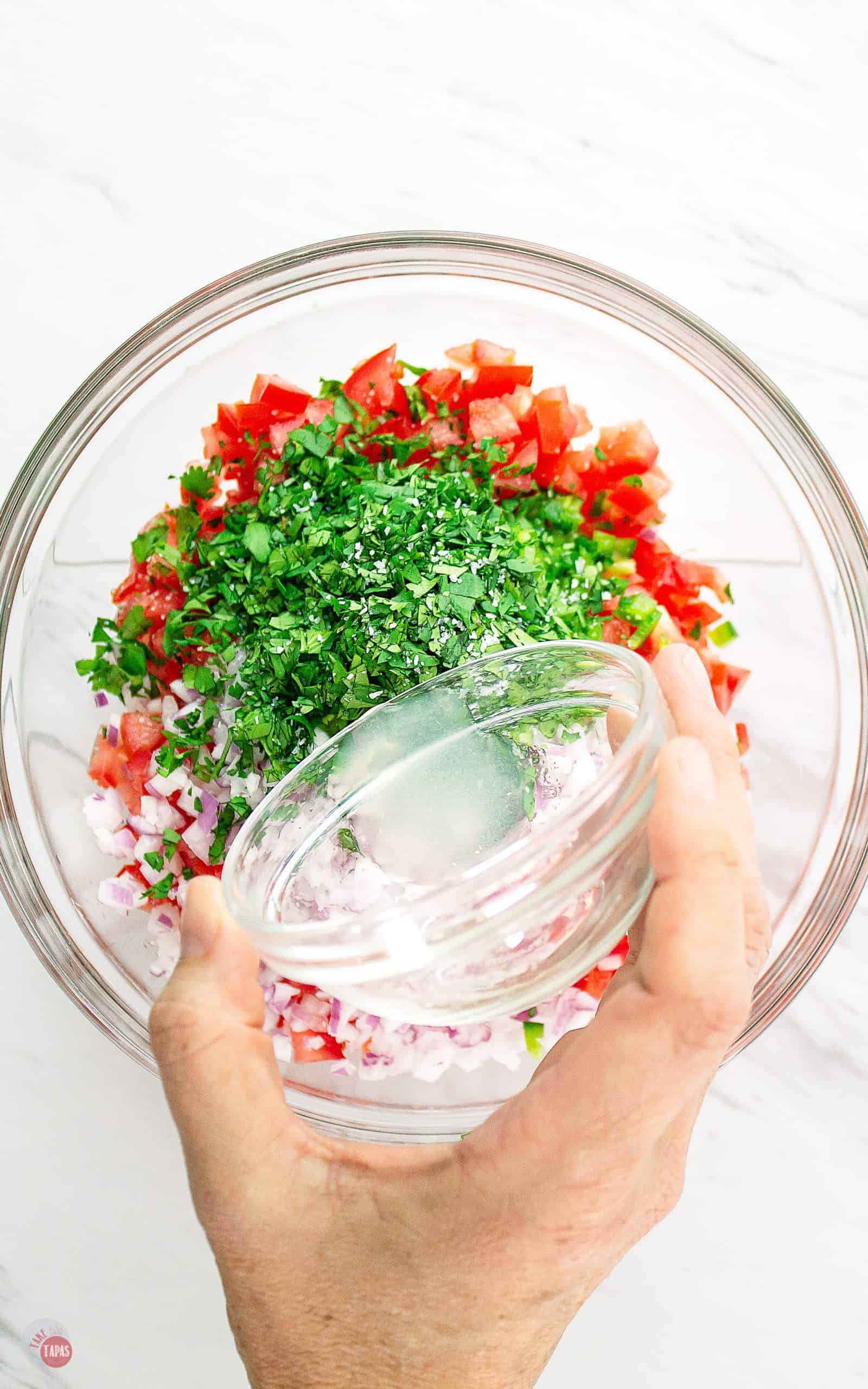 lime juice being poured into a bowl of pico ingredients