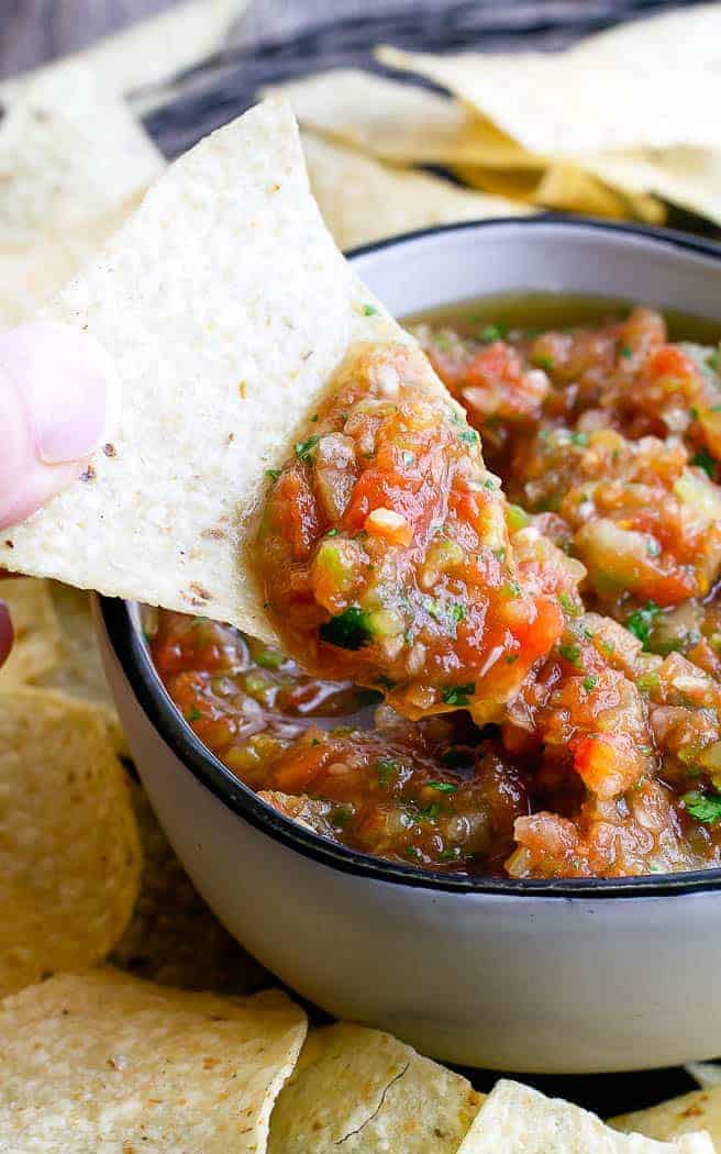 white bowl with salsa surrounded by chips with a hand scooping out salsa