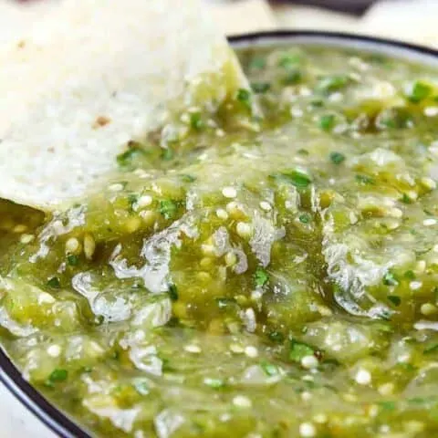 close up of a white bowl of green salsa with a tortilla chip sticking out of it