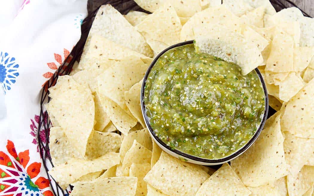 overhead view of green salsa in a bowl surrounded by chips