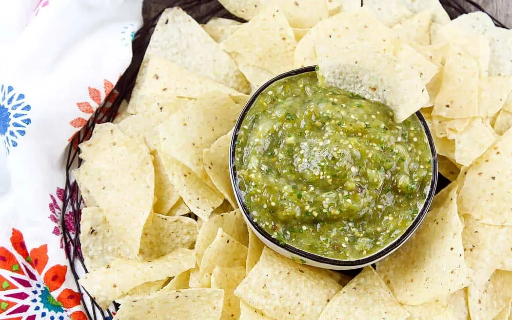 overhead view of green salsa in a bowl surrounded by chips