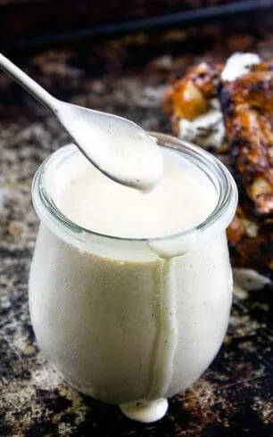 spoon dripping white bbq sauce into jar