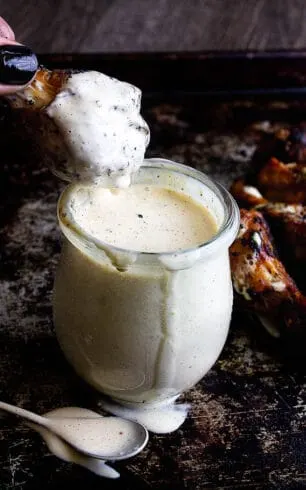 chicken wing dipping in a jar of white sauce