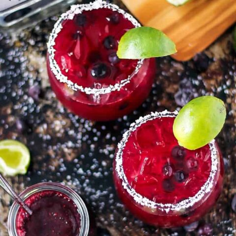 Overhead of 2 blueberry margaritas on a dark surface