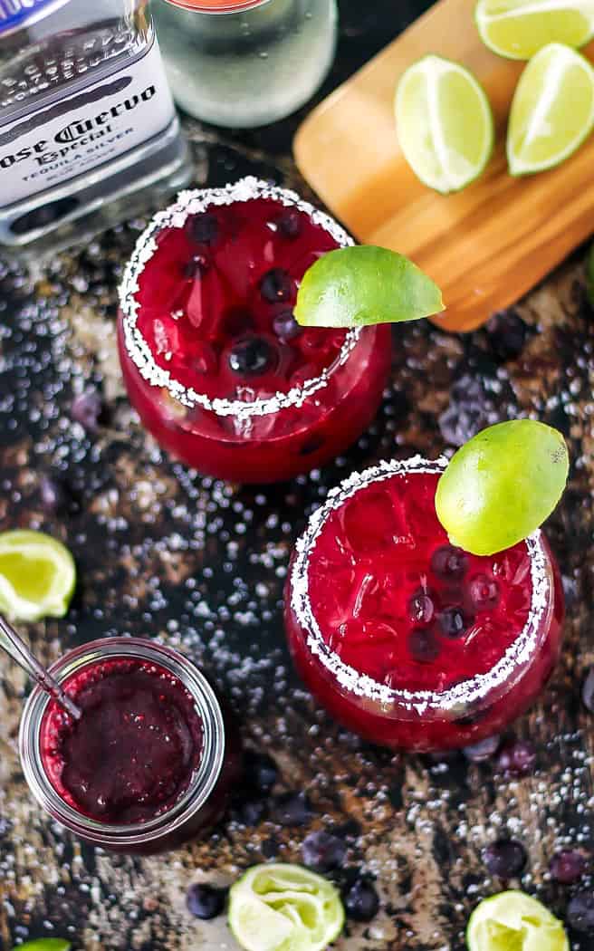 Overhead of 2 blueberry margaritas on a dark surface