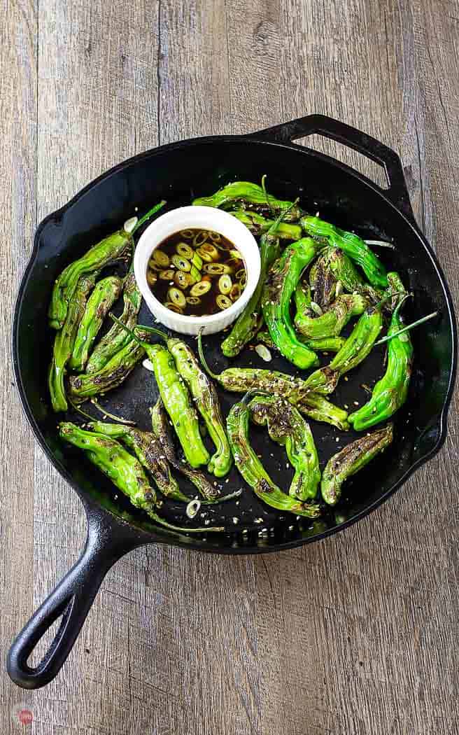 overhead picture of roasted shishito peppers in a cast iron skillet with white bowl of dipping sauce