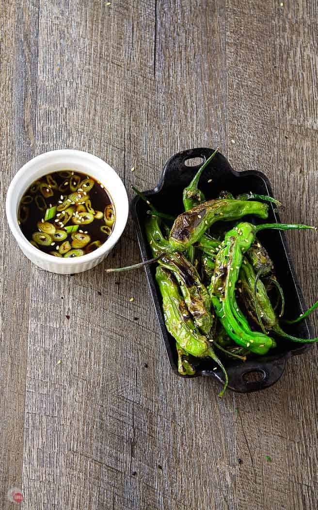 overhead picture of roasted shishito peppers in a cast iron dish with white bowl of dipping sauce