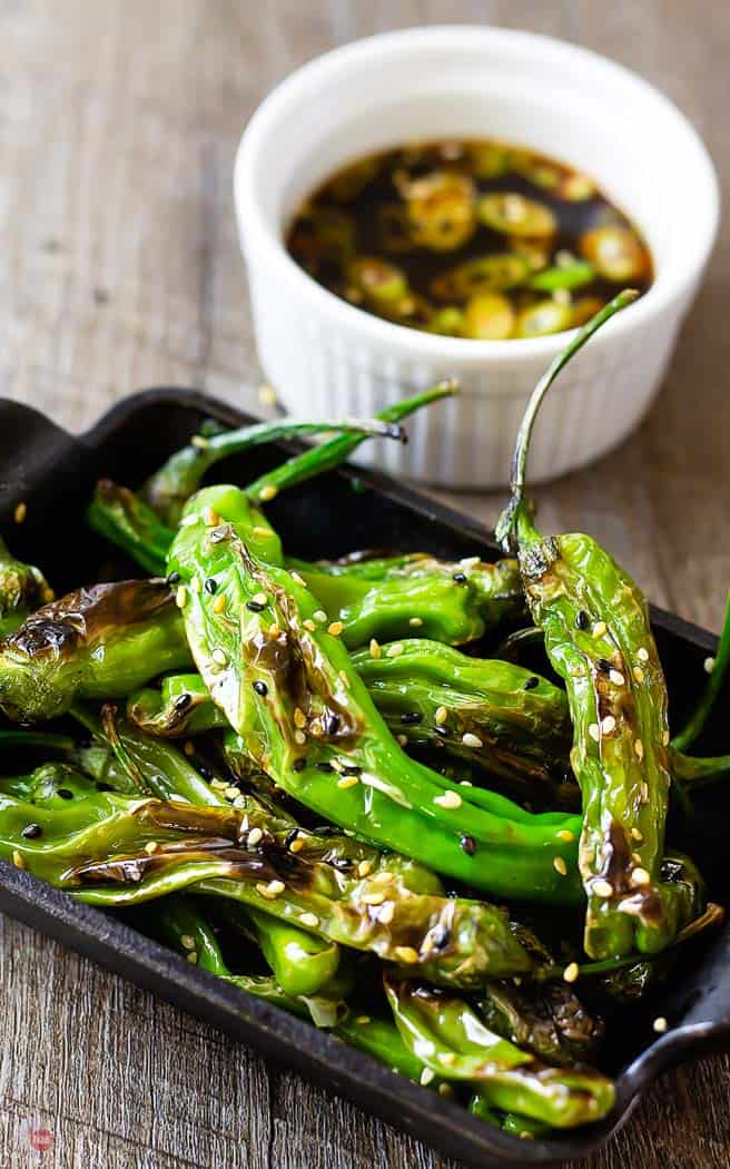 roasted shishito peppers in a cast iron dish with white bowl of dipping sauce