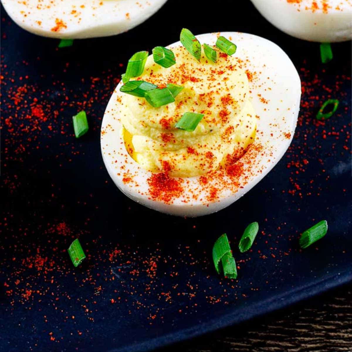 deviled egg with paprika and chopped chives garnish on a black plate