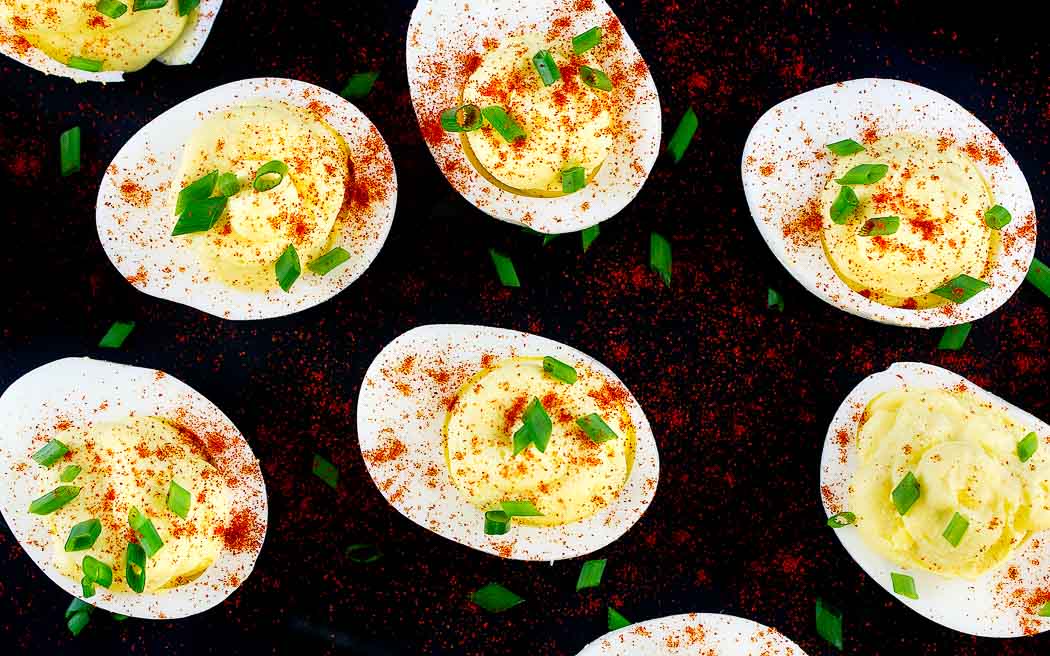 overhead picture of deviled eggs on a black platter with chive garnish