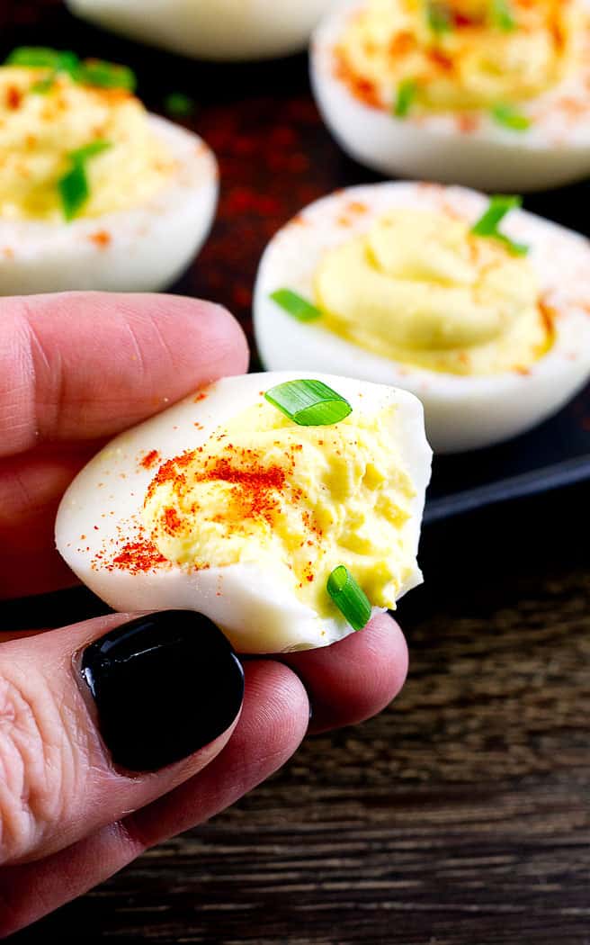 hand holding a deviled egg with a bite out of it