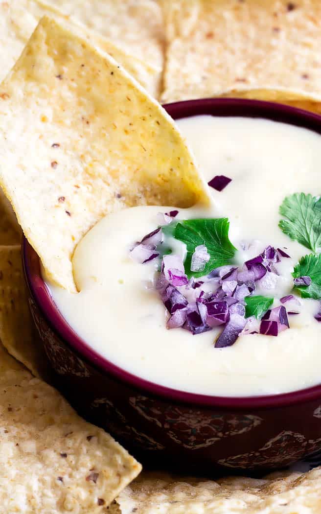 close up of cheese dip with toppings and a chip in it