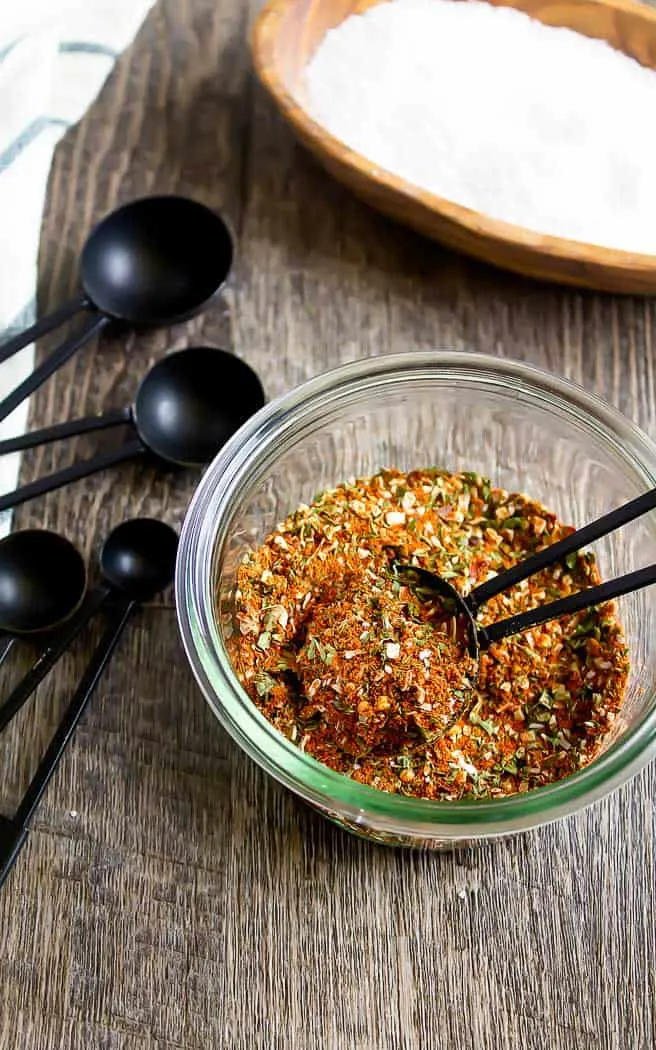 overhead picture of a jar of southwest seasoning spices with a spoon in it with 4 black measuring spoons and a napkin on the left