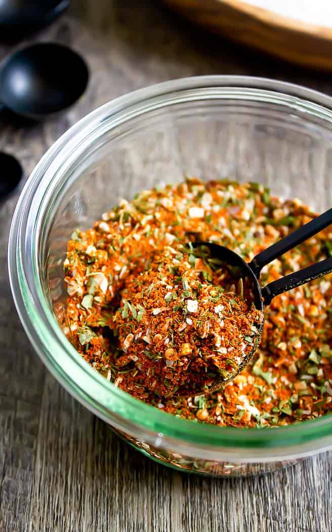 southwest seasoning in a glass jar with a black measuring spoon in it with a bowl of salt in the back